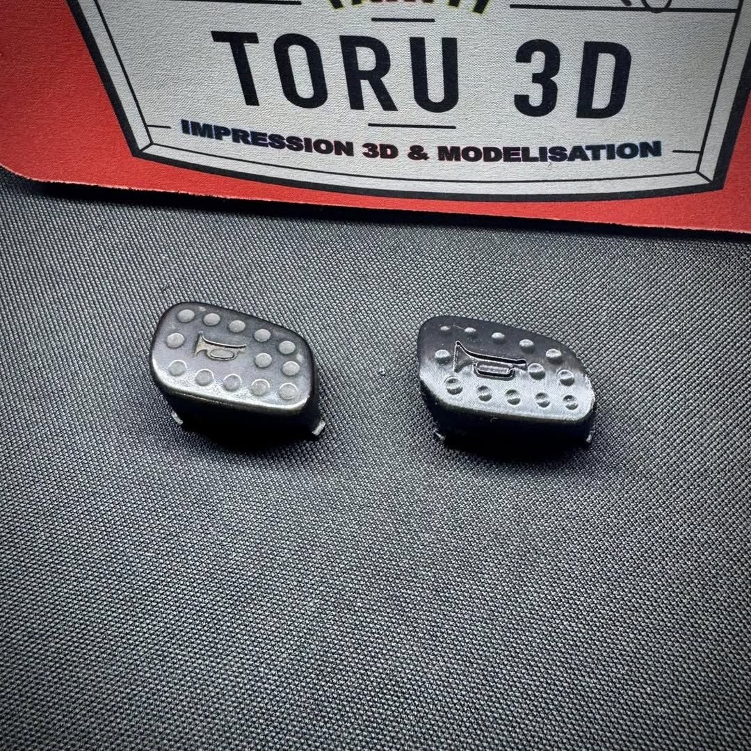 Deux caches noirs imprimés en 3D posés sur un tapis, devant le badge Toru 3D